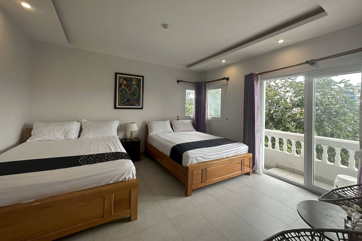 Un dormitorio con dos camas, un cuadro en la pared y un balcón con vistas a zonas verdes.