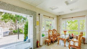 A spacious room with large windows, a wooden dining table, and matching chairs. - Capital O 1207 Green Hill Villa Da Lat (Xuan Truong - Da Lat)