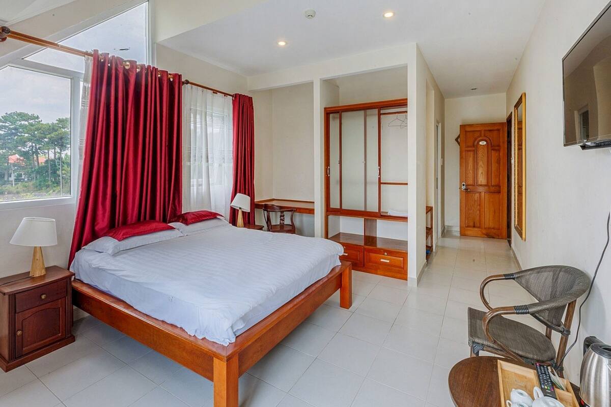 Habitación de hotel con una cama grande, un armario de madera, un escritorio con lámpara, una silla y un televisor montado en la pared.