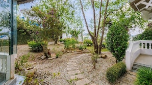 A garden with a stone pathway, trees, and a white building with a balcony. - Capital O 1207 Green Hill Villa Da Lat (Xuan Truong - Da Lat)
