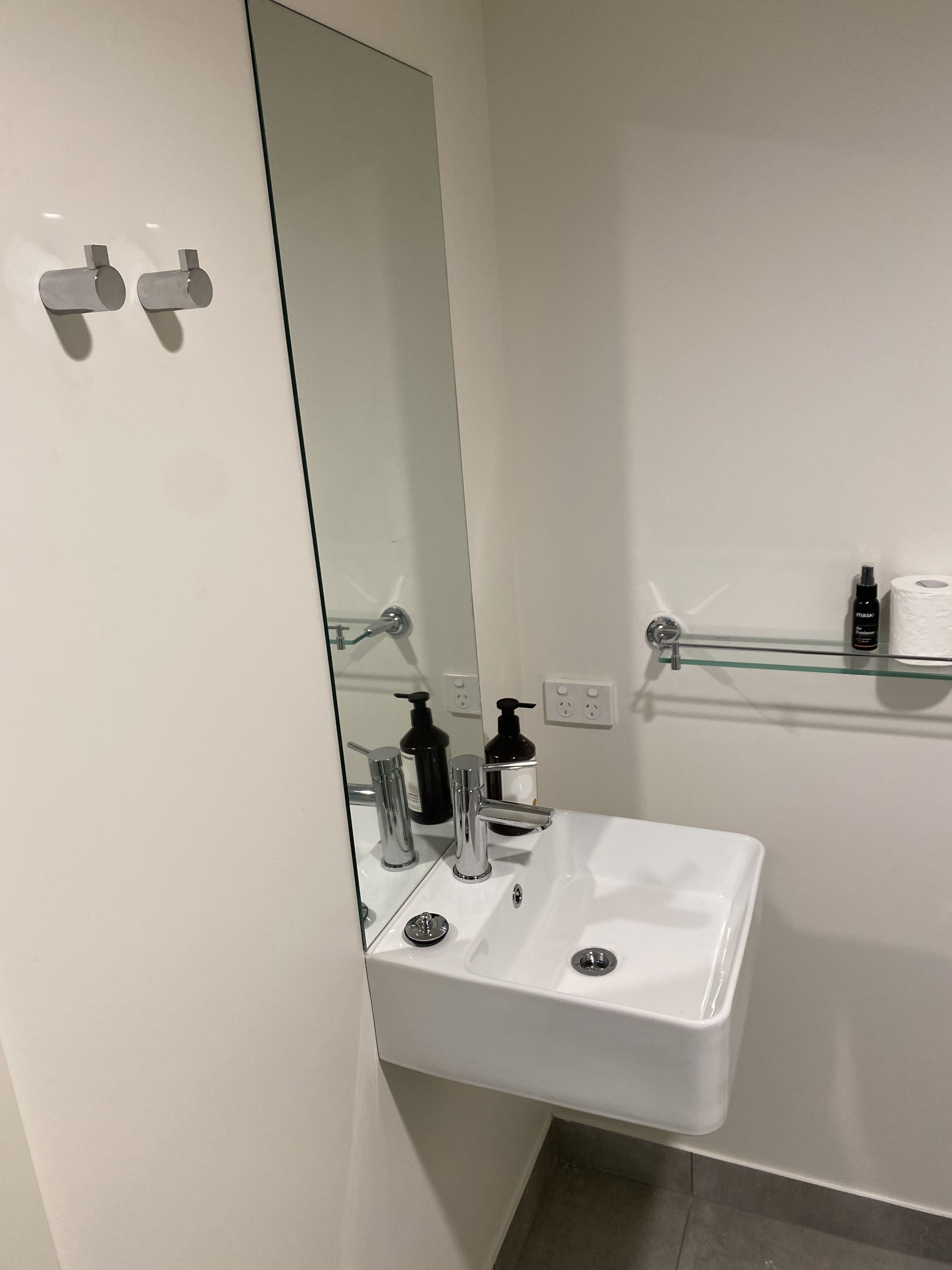 A modern bathroom with a white sink, chrome fixtures, and a glass shelf holding toiletries.