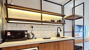 A modern kitchen with a microwave, kettle, and coffee maker on the counter, wooden cabinets, and a built-in shelf above the sink. - Expressionz Premium Suites at KLCC (Kuala Lumpur)