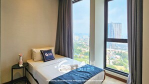 A hotel room with a large window, a bed with a pillow, a small table with a vase, and curtains. - Expressionz Premium Suites at KLCC (Kuala Lumpur)
