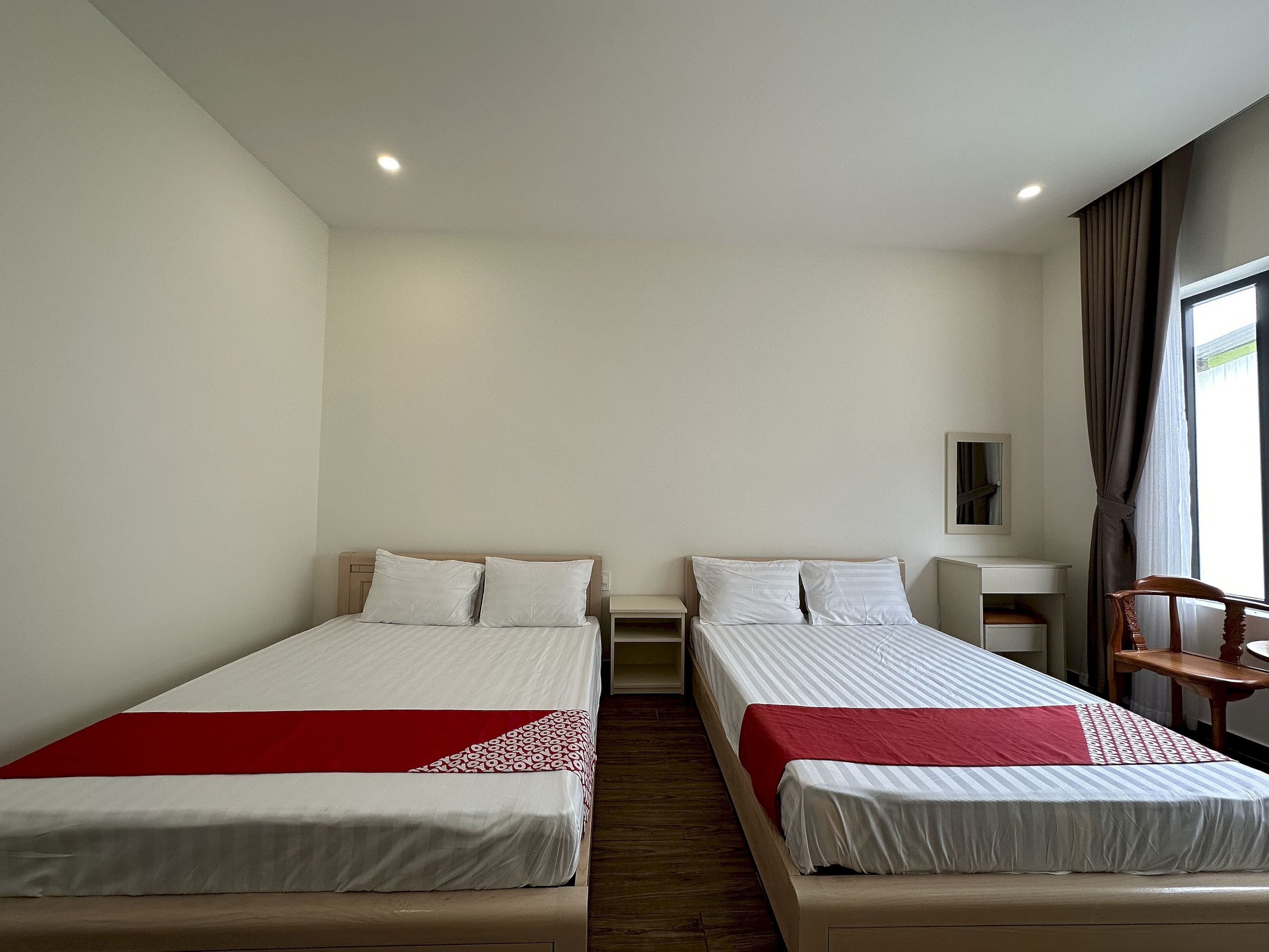 A hotel room with two beds, a desk, a chair, and a window with curtains.