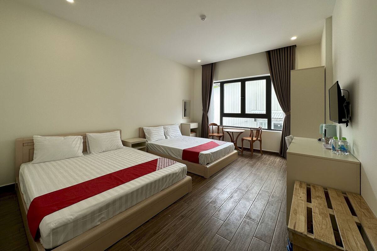 A hotel room with two beds, a desk, a chair, a TV, and a window with curtains.