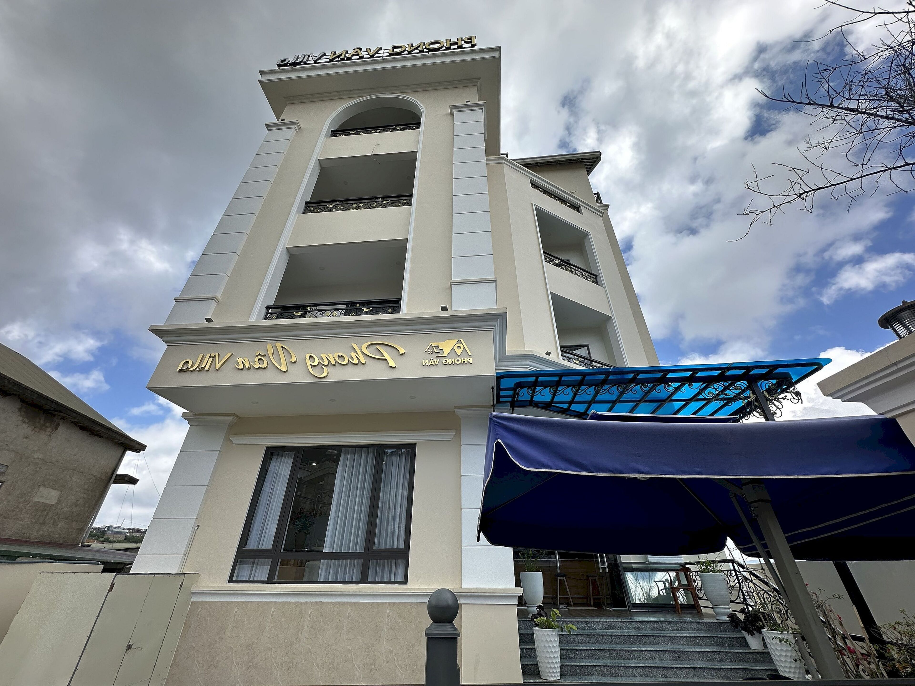 Un hotel de varios pisos con un cartel llamativo en un idioma extranjero, ventanas amplias y un toldo azul sobre la entrada.