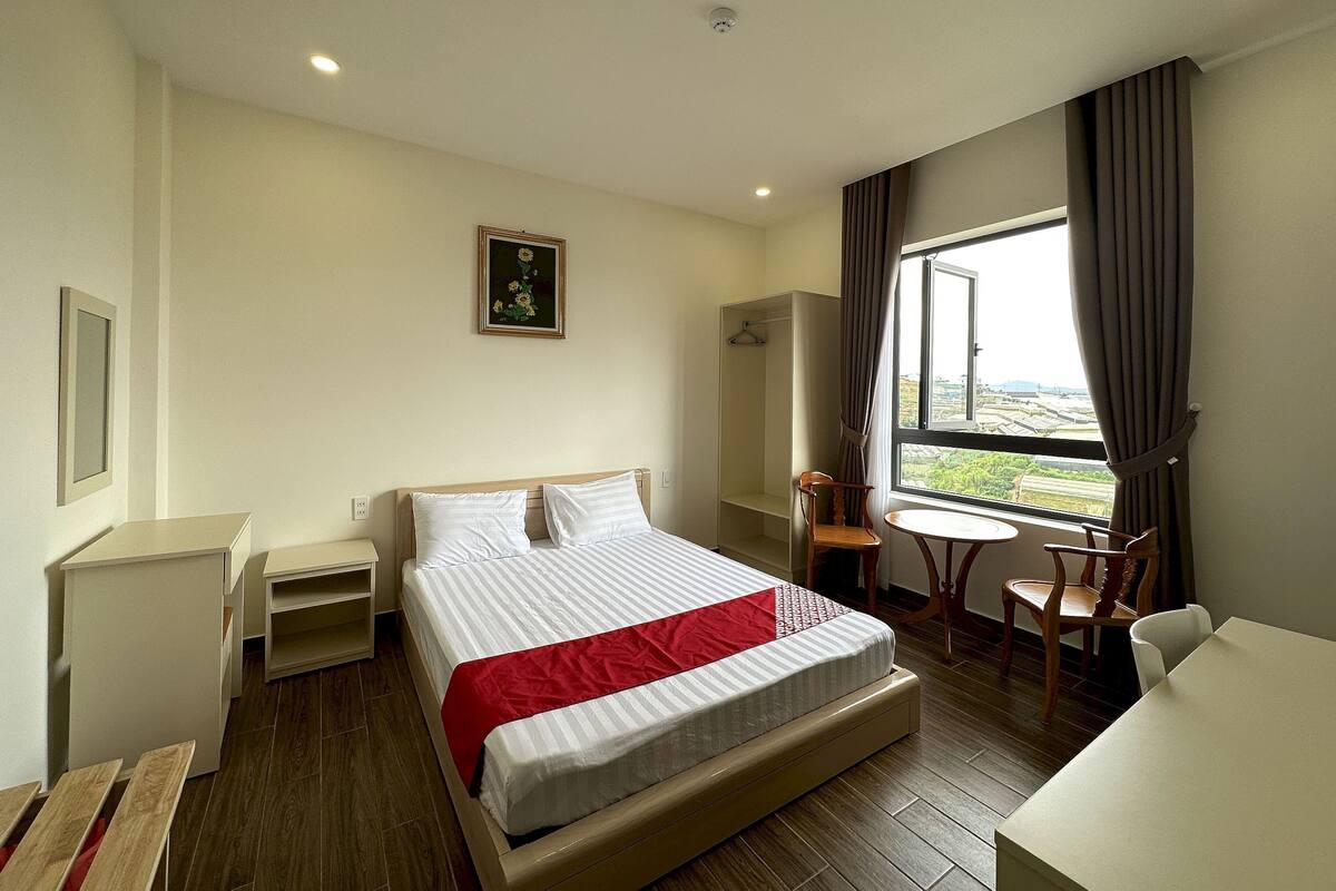 A hotel room with a bed, a desk, a chair, a small table, a wardrobe, and a window with curtains.