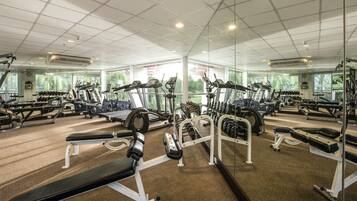 Un gimnasio con diverso equipo de ejercicio, ventanas amplias y techo de baldosas.