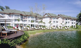 Un resort con edificios de varios pisos, una zona de piscina con tumbonas y una pequeña masa de agua.