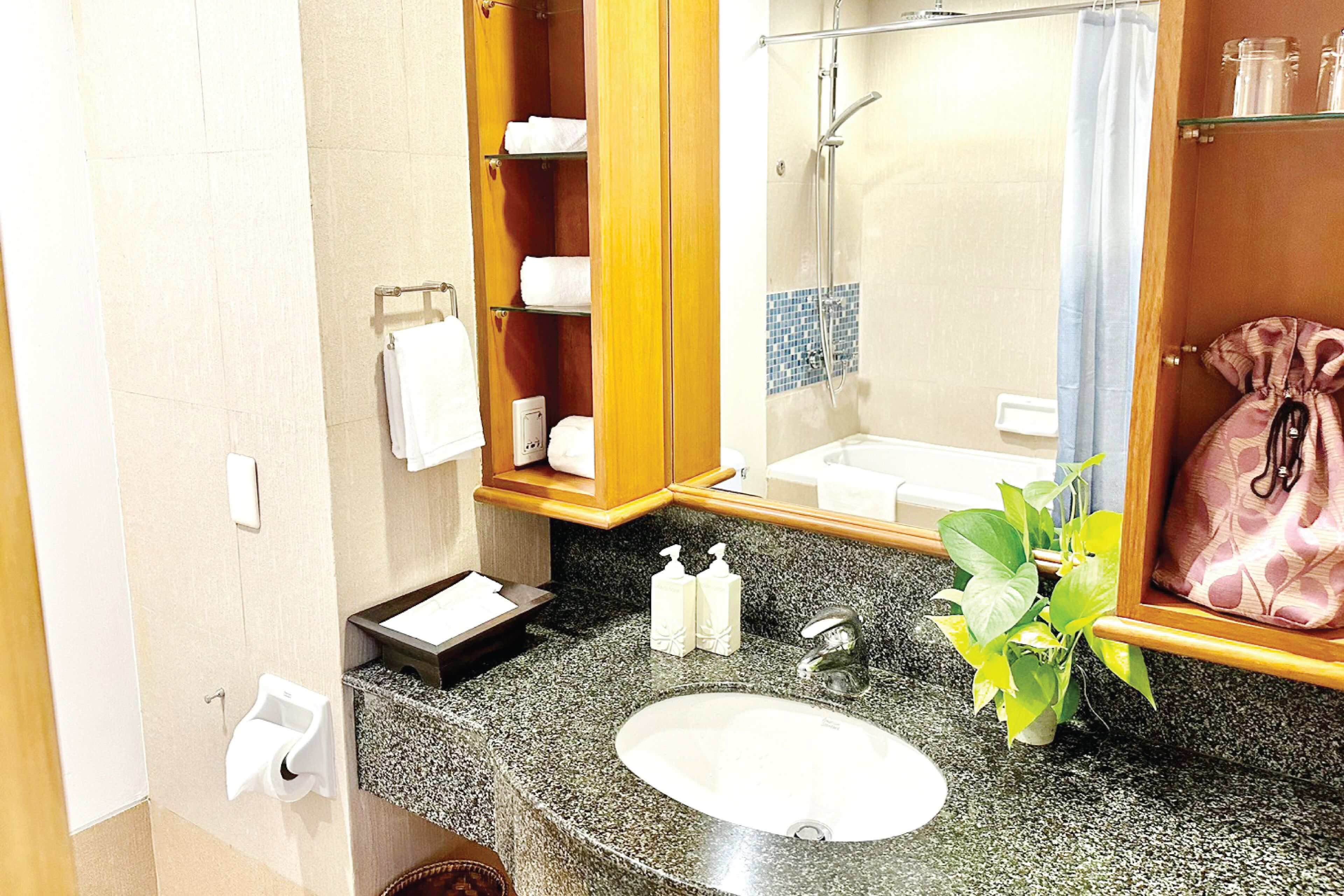 Un baño con lavamanos de encimera de granito, un espejo, ducha y toallero.