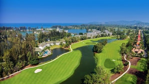 A golf course with a water body, surrounded by trees and buildings. - Homm Suites Laguna, part of Banyan Group (Choeng Thale)