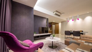 A modern living room with a purple armchair, a sofa set, a flat-screen TV, and a dining area with chairs and a table.