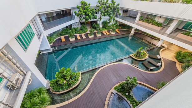 A rooftop pool area with multiple swimming pools, surrounded by wooden deck areas and lush greenery.