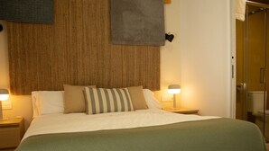 Una cama bien hecha con un edredón verde, dos lámparas de noche y un cabecero tejido.