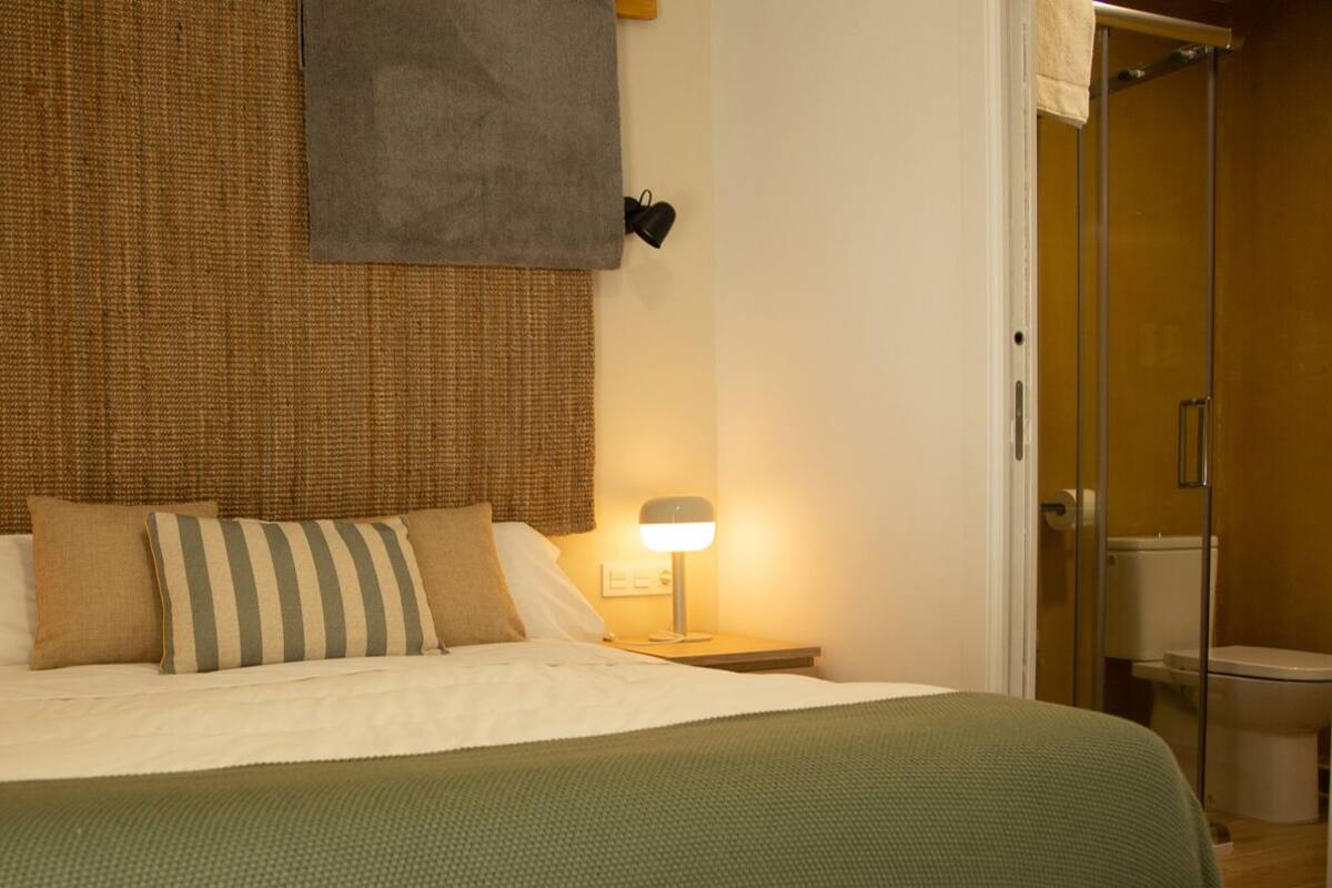 A neatly made bed with a green blanket, two bedside lamps, and a woven headboard.