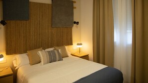 Una habitación de hotel con una cama grande, dos mesitas de noche, una lámpara y un ventanal con cortinas.