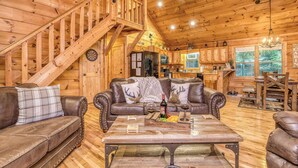 A wooden cabin interior with a loft bedroom, a dining area, and a kitchen.