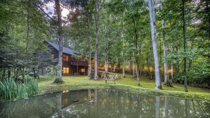 A cabin with a deck and a pond, surrounded by trees.