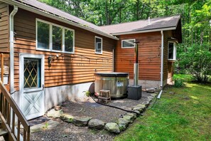 A wooden cabin with a hot tub, a small wooden stool, and a stone pathway leading to the door.