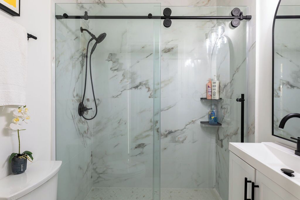 Een moderne badkamer met een douchecabine van glas, marmeren wanden, een witte wastafel en een spiegel.