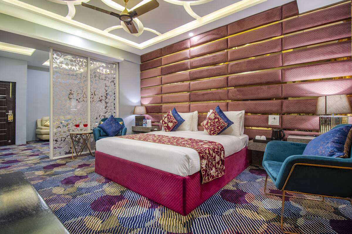 A modern bedroom with a large bed, a ceiling fan, a nightstand, a chair, and a decorative wall panel.