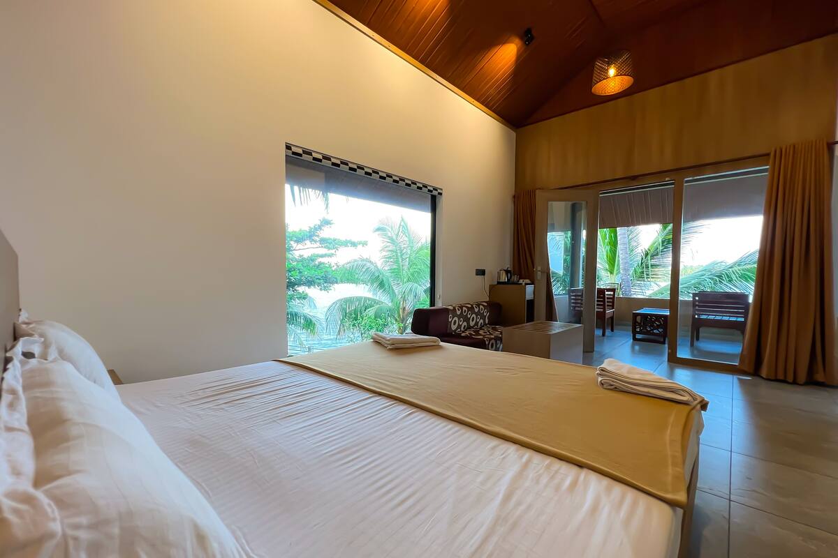 A bedroom with a large bed, a sofa, and a view of a balcony with outdoor furniture.