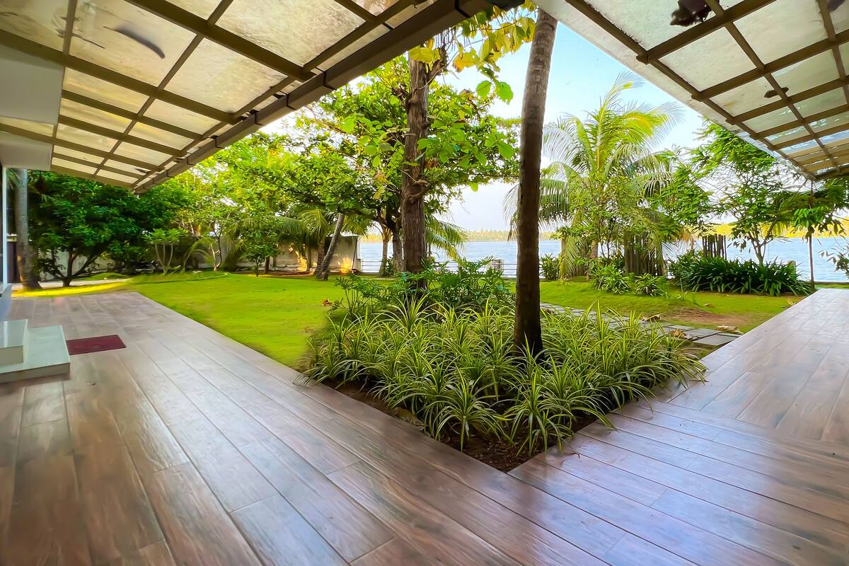 A covered outdoor area with a wooden deck, a grassy lawn, and a view of a body of water.
