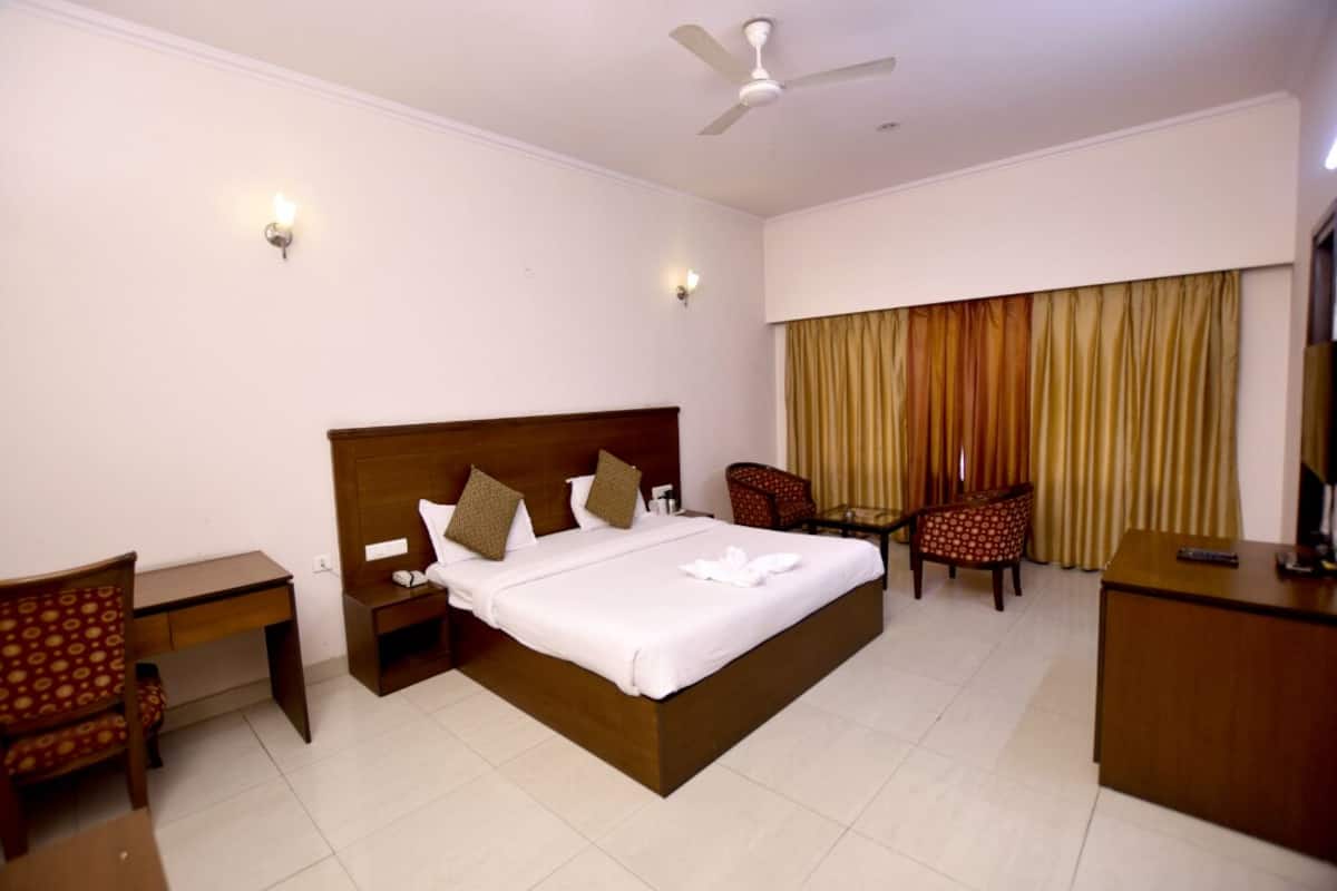 Quarto de hotel com uma cama grande, duas mesas de cabeceira, uma escrivaninha, uma cadeira, televisão e ventilador de teto.
