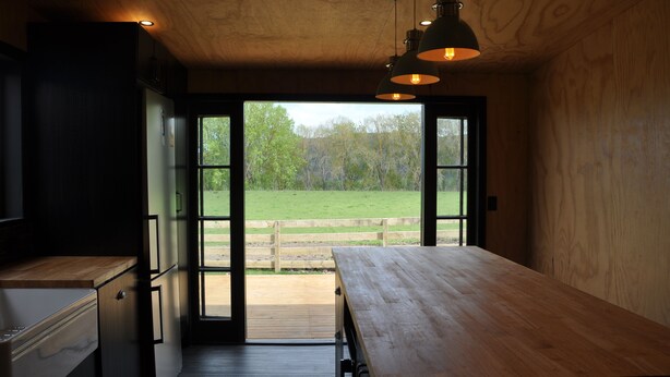 A modern kitchen with wooden cabinets and a large window leading to an outdoor area. - Renagour Cottage - Rural charm with outdoor hot tub! (Mangamahu)