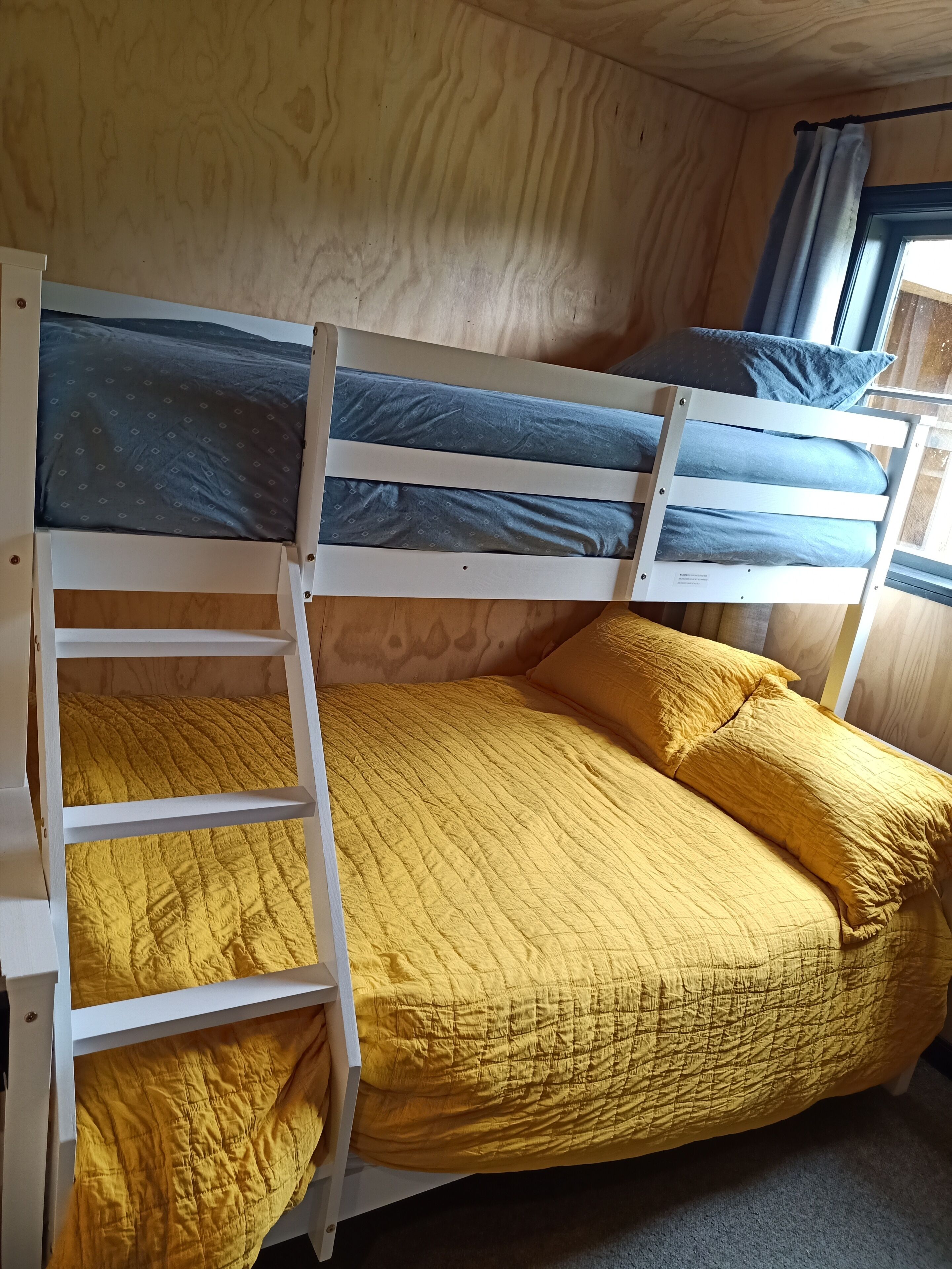 Ein Stockbett mit gelber Bettwäsche und einem Fenster mit Vorhängen.