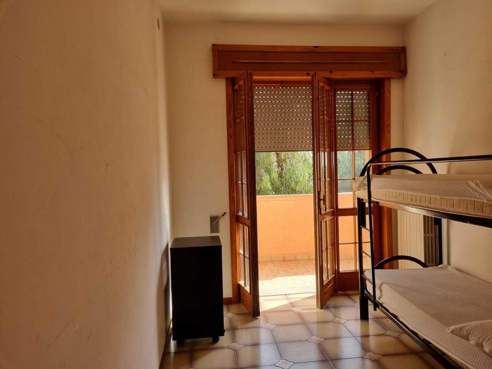 Una habitación pequeña con una cama individual superpuesta, una puerta que da a un área exterior y un mueble negro pequeño.
