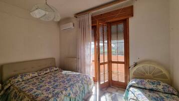 Un dormitorio con dos camas, un radiador, un equipo de aire acondicionado y una ventana con cortinas.