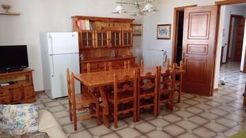 A living room with a wooden dining table, chairs, a sofa, a television, and a built-in wooden cabinet.