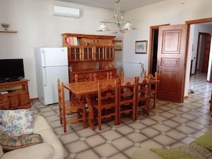 A living room with a wooden dining table, chairs, a sofa, a television, and a built-in wooden cabinet. - Casa Vacanze Nonno Gino Home (Nardò)