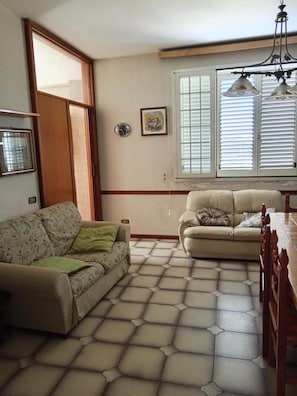 A living room with two sofas, a dining table, a window with blinds, a wall clock, and a framed picture. - Casa Vacanze Nonno Gino Home (Nardò)