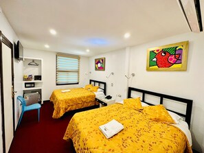 A hotel room with two beds, a desk, a chair, and artwork on the walls.