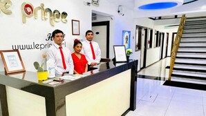 Una mesa de recepción con tres empleados, un certificado enmarcado y un cactus en la encimera.