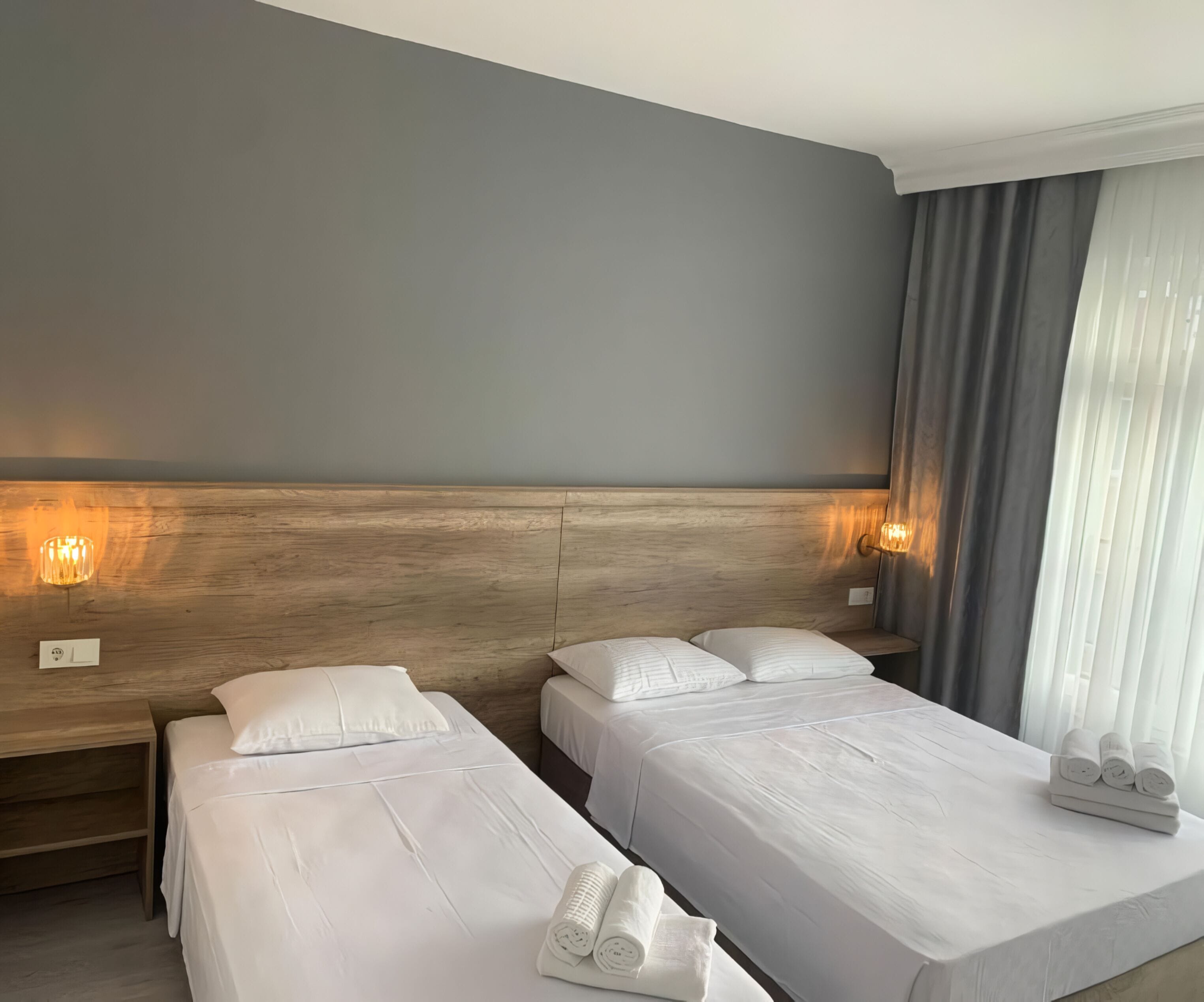 Ett hotellrum med två separata sängar, en sänggavel i trä, ett nattduksbord och en lampa.