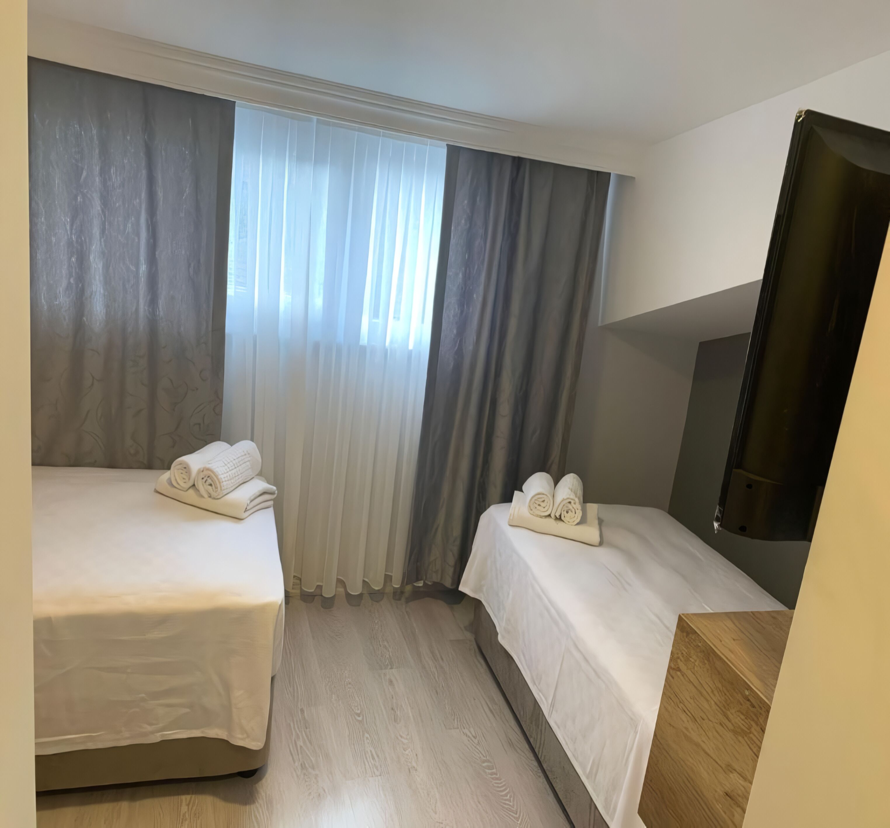 A hotel room with two beds, a TV, and a large window with curtains.