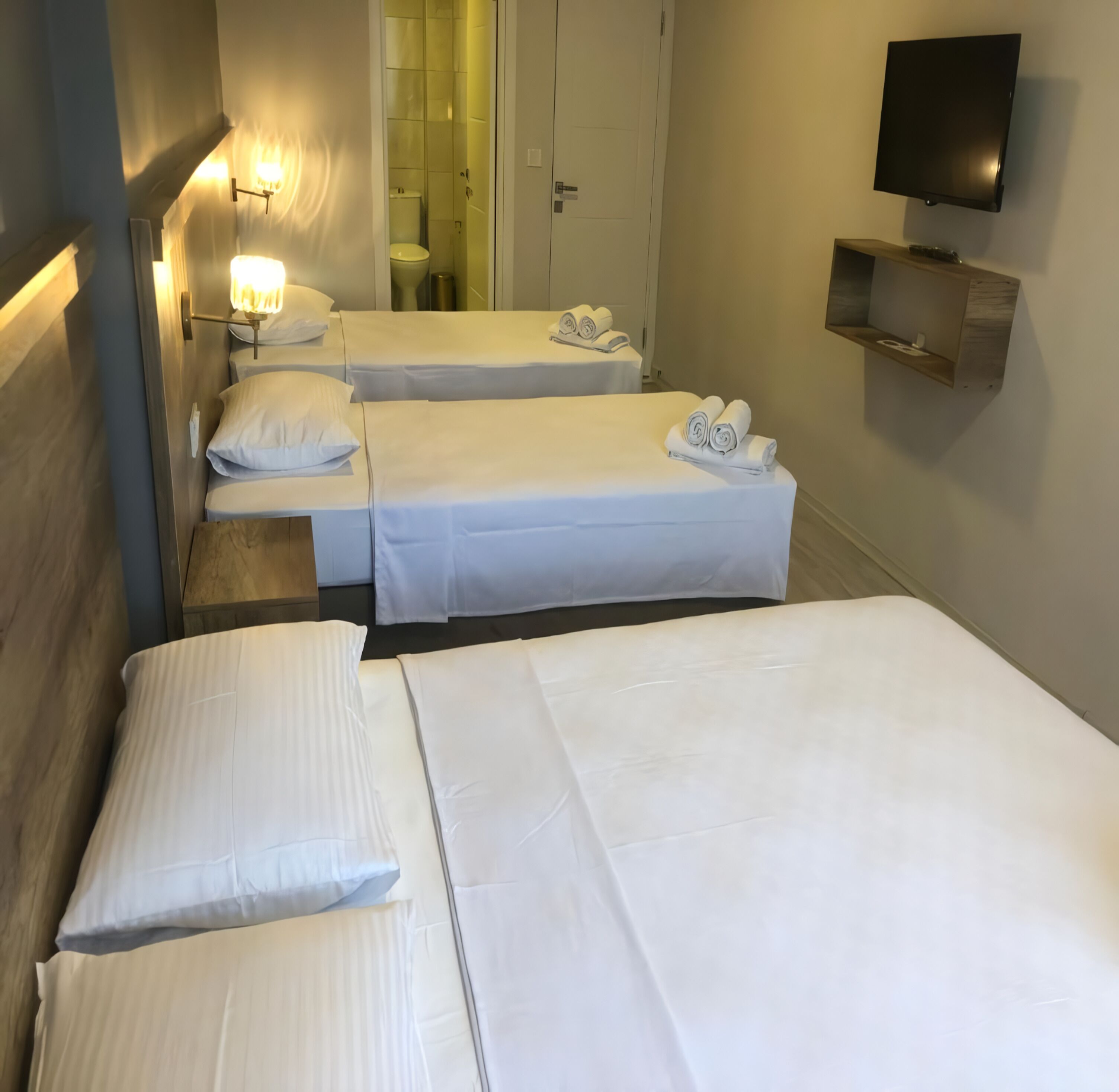 Una habitación de hotel con tres camas, un televisor montado en la pared y un pequeño estante.