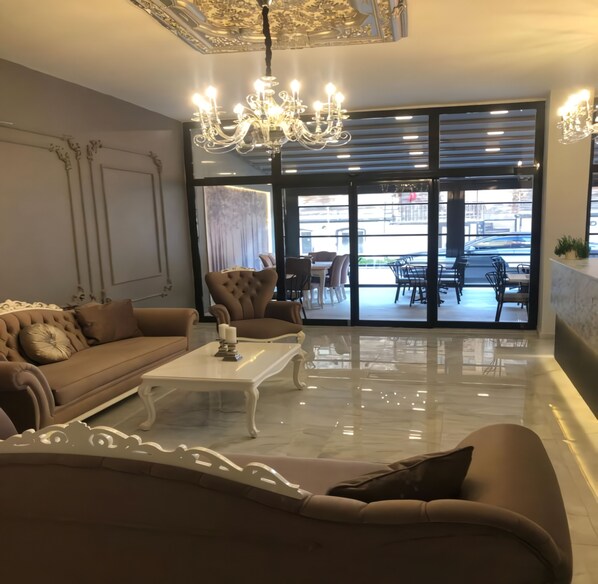 A modern living room with a brown sofa, a white coffee table, and a chandelier. - Rinascente (Edirne)