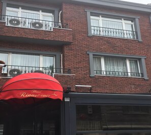 A red awning with "Hotel Rinascente" written on it, a brick building with multiple windows and balconies, and a garage door. - Rinascente (Edirne)
