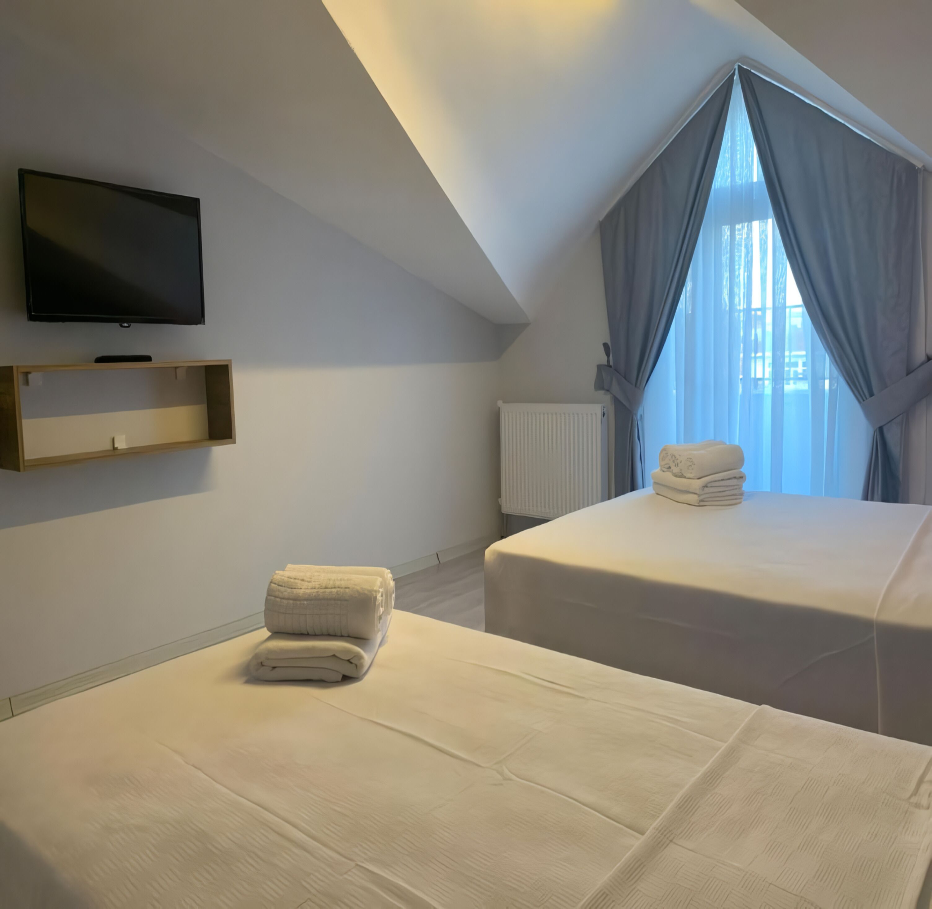 Habitación de hotel con dos camas, televisión y ventana con cortinas.