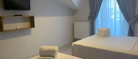 Habitación de hotel con dos camas, televisión y ventana con cortinas.