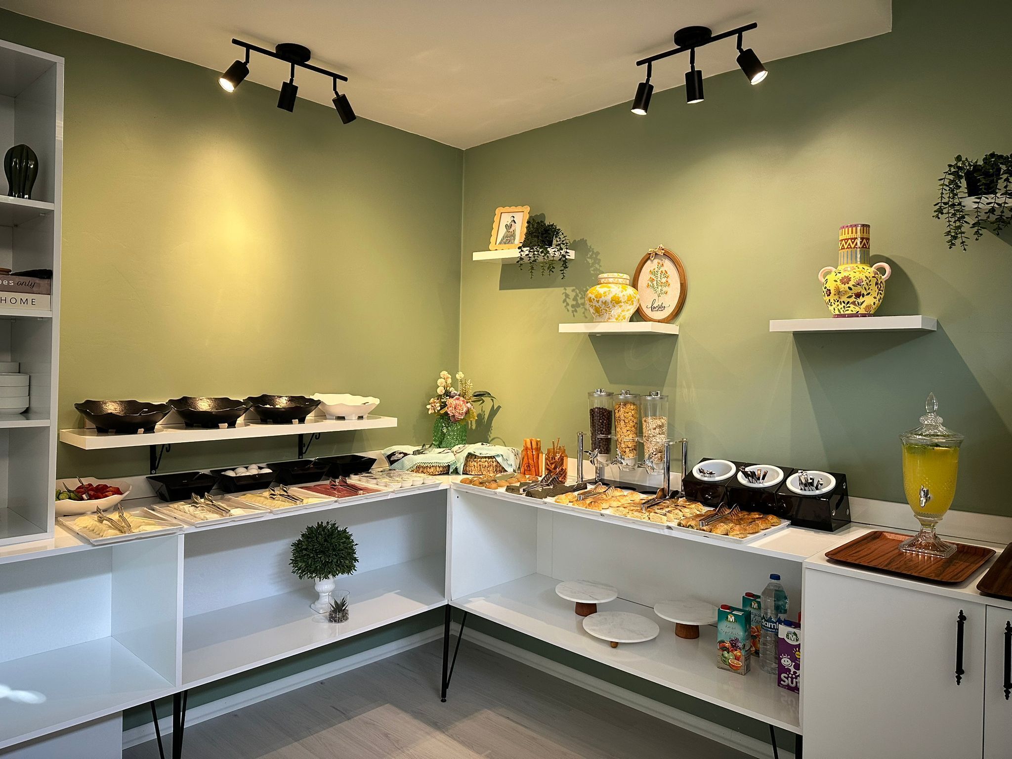 Montaje de bufé con diferentes alimentos y bebidas, incluyendo recipientes, bandejas y un dispensador de zumo.