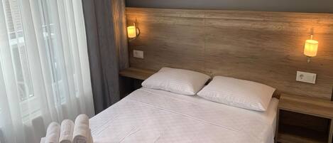 Una habitación de hotel con una cama grande, dos mesitas de noche y un ventanal con cortinas.