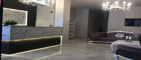 A modern lobby with a marble reception desk, a chandelier, a sofa, and a television.