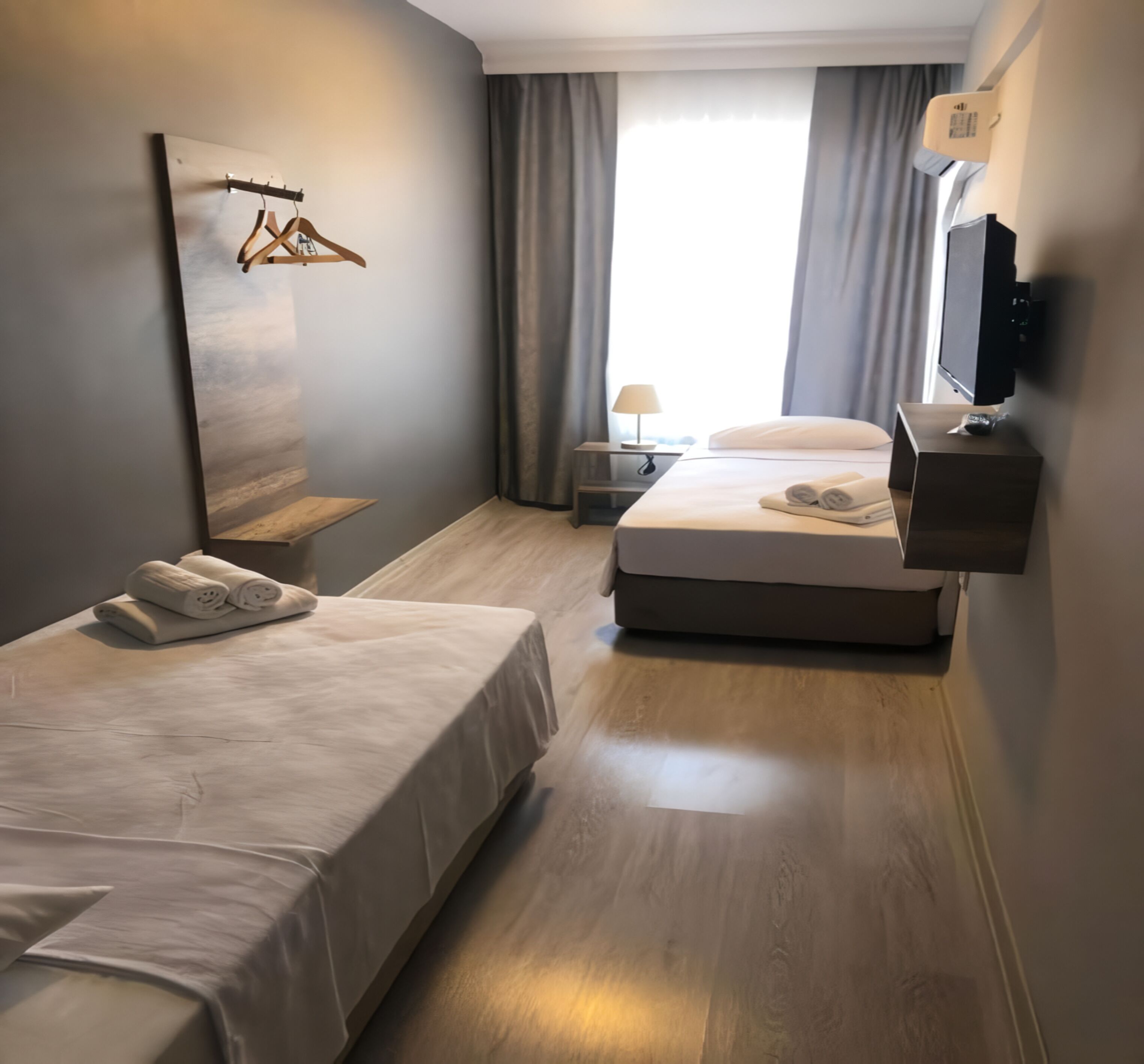 Ein modernes Hotelzimmer mit einem großen Bett, einem kleineren Bett, einem an der Wand befestigten Fernseher und einem Gemälde an der Wand.
