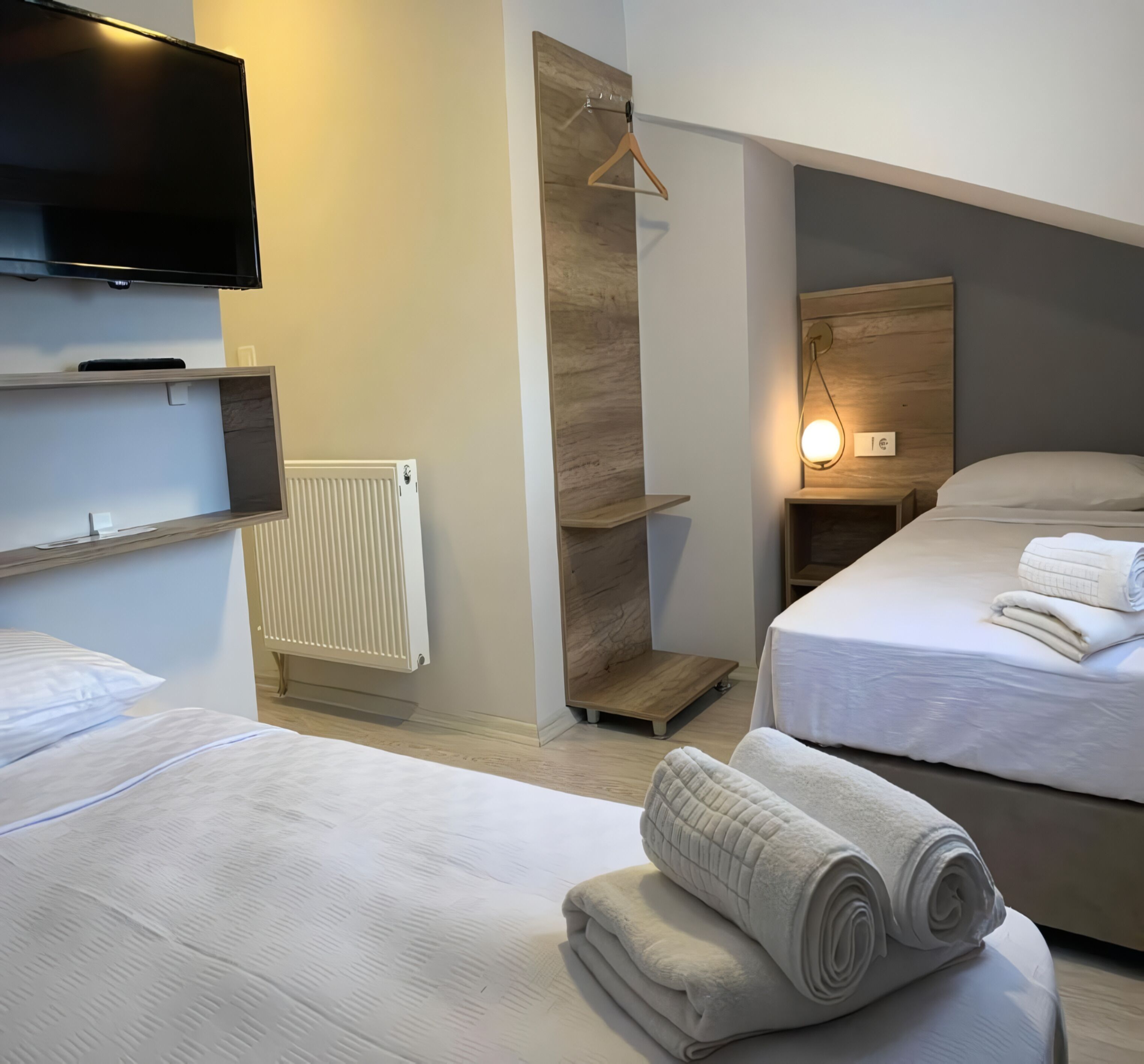 Habitación de hotel con dos camas, un televisor, un radiador y un estante de madera.