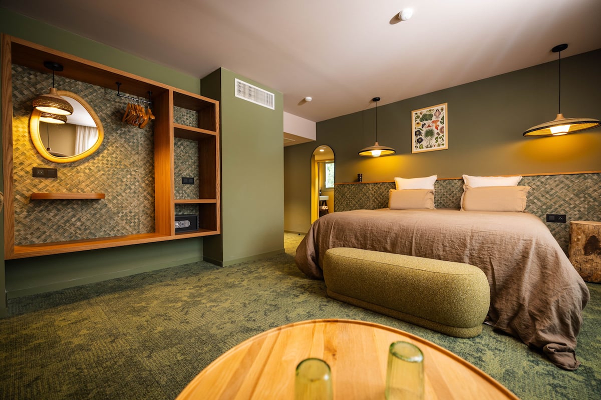 Une chambre à coucher avec un grand lit, un banc en bois, un miroir et une étagère contenant des articles de toilette.